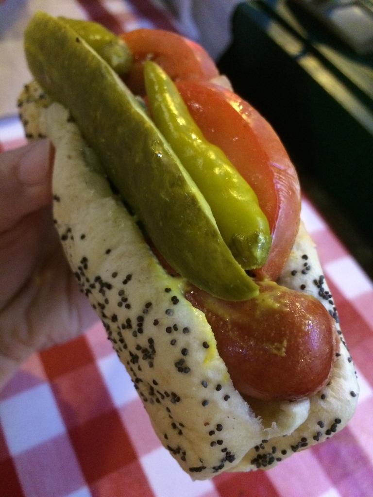 A Chicago dog is dragged through the garden because of the vegetable toppings: dill pickle spear, relish, sport peppers, tomatoes, and onions.  Celery salt and mustard top it off, but no ketchup!